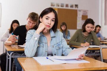 Smiling young schoolgirl is sitting test and answer about task in the classroom.