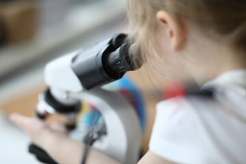 Close-up of cute child investigating sample under modern microscope. Kid having fun with research indoors. Spare time with exploration. Funny science and childhood concept