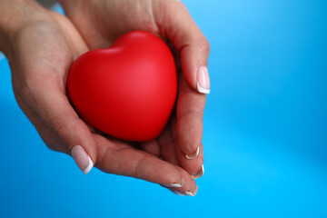 Close-up of female hands holding red heart on blue background. Motherhood and protection. Copy space. Family relationship and charity and adoption concept