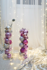 Purple bulbs in transparent glass vase. Christmas and New Year decorations and toys. Blurry white background with warm garland lights and bokeh. Winter magic. Place for text. Vertical shot.