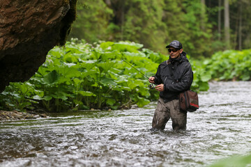 Naklejka premium A fisherman walking for wild river and a breathtaking scene in the forest with colourful reflections on the river. Fishing day hunting for a trout. Finding solitude in the wilderness.