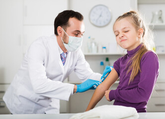 Male doctor using syringe to make injection to young female patient in hospital