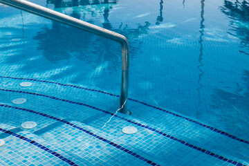 Pool stairs water blue. Step down to the pool. Railing and stairs to the pool. Selective focus 