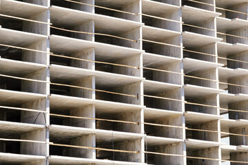 Detail of residential building under construction. Concrete structure with metal struts and temporary wooden railings. High-rise residential building under construction against a blue sky with clouds