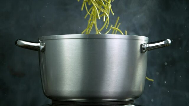 Throwing pasta pappardelle into boiled water in steel pot, shooting with high speed cinematic camera at 1000 fps.