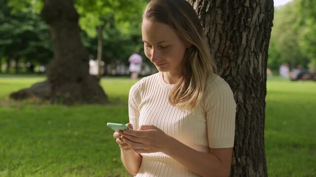 Close up of a beautiful young woman, that is using an application in her smart phone in park. Communicate about phones, technology, applications
