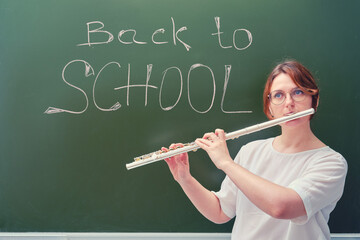 Music teacher plays flute near blackboard with text "Back to school"