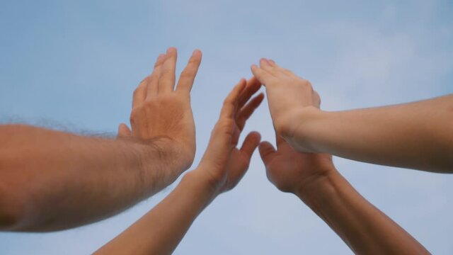 A group of successful people raise their hands up and hold hands against the blue sky, together they are a successful team. A happy family in a team joins hands for successful work and collaboration.