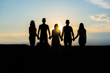 Cohesion concept. Black silhouettes of friends holding hands stands at sunset.