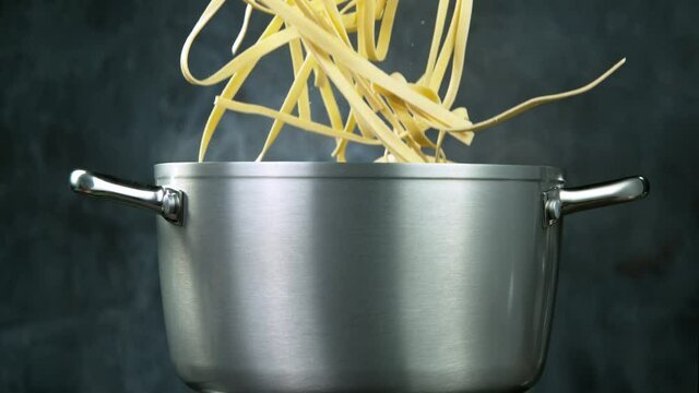Throwing pasta pappardelle into boiled water in steel pot, shooting with high speed cinematic camera at 1000 fps.