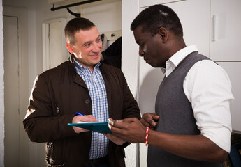 Friendly landlord visiting tenant apartment, signing agreement with positive man - obrazy, fototapety, plakaty