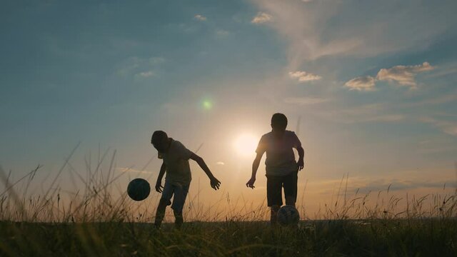 Teamwork. Two boy friends play soccer at sunset. Happy family. Silhouette of children playing with a ball at sunset.