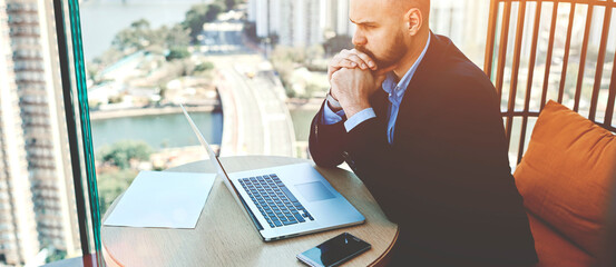Concentrated and worried businessman sitting front open net-book in his office, male entrepreneur...