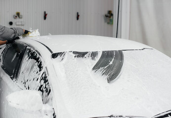 Modern washing with foam and high-pressure water of a white car. Car wash
