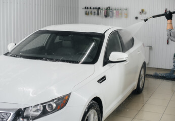 Modern washing with foam and high-pressure water of a white car. Car wash