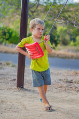 Sad lonely boy sit on swing look far away, wait for friends or while parents are busy, thinking about important things for him. Summer, childhood, leisure, friendship, relationship and people concept