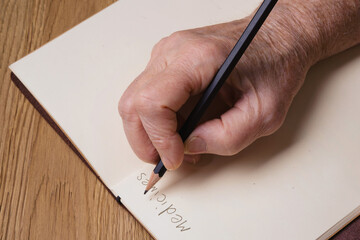 Elderly woman's hands holding a pencil and writing the word 