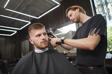 Low angle shot of a man getting a haircut by professional barber at the salon