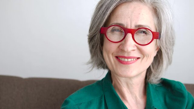 Grey-haired woman in fashionable glasses smiling to camera, femininity, trends