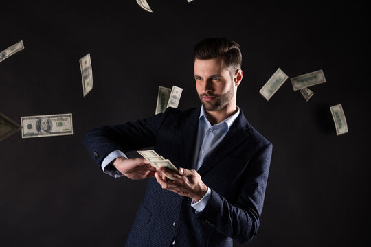 Photo of handsome business guy hold hands usa bucks rich success millionaire throwing banknotes spend money generous wear blue costume blazer shirt isolated black color background