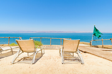 Rear view of two lounge chairs or tanning beds set on a sand terrace in a beach resort, overlooking the Dead Sea and Israel territories near Madaba, Jordan, Middle East