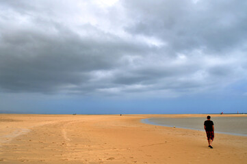 a man walks on a beautiful lonely beach with dark clouds in the sky, Sotavento, Fuerteventua, Canari Islands, Spain