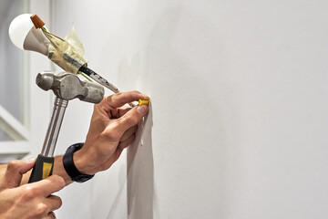 Close up of worker clogs a dowel into a wall using a hammer to install a new lamp in the house - obrazy, fototapety, plakaty