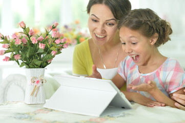 Happy mother and daughter using tablet together at home