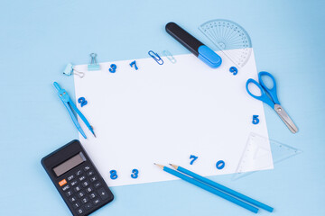 on a blue background, numbers, calculator, ruler, marker, paper clips, compasses, scissors and a white sheet of paper