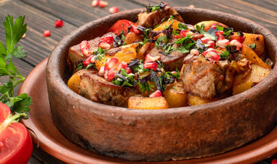 Fried potatoes with meat and pomegranate seeds, in a clay plate, on a wooden background with herbs and tomato