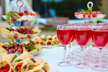 A row of glasses with red drinks, juice, champagne or wine at a party. Catering. Glassware on the table with a white tablecloth. Festive buffet for the holiday.