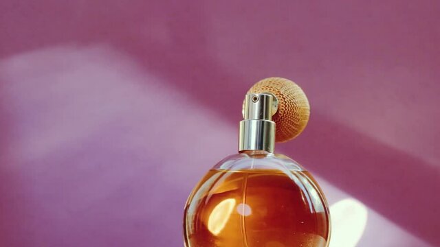 Luxury golden perfume bottle and shining light flares on pink background, glamorous fragrance scent as perfumery product for cosmetic and beauty brand, stock footage