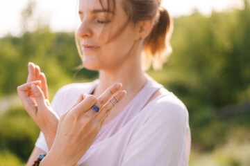 Obraz premium Close-up of face of calm young meditating woman standing on nature with closed eyes holding crossed hands on her chest in yoga posture mudra. Concept of practicing yoga alone outdoor.