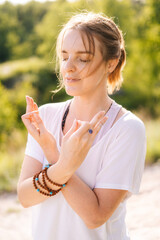 Portrait calm young meditating woman standing on nature with closed eyes holding crossed hands on her chest in yoga posture mudra. Concept of practicing yoga alone outdoor.