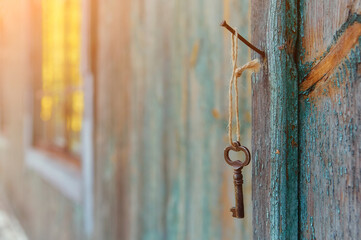 An old iron retro key hanging on a nail against the wall of a rustic wooden house, the concept of a...