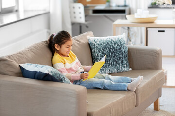 childhood and leisure concept - happy smiling little girl reading book at home