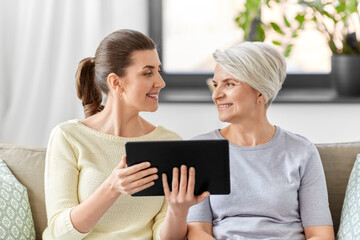 family, generation and technology concept - happy smiling senior mother and adult daughter with tablet pc computer at home