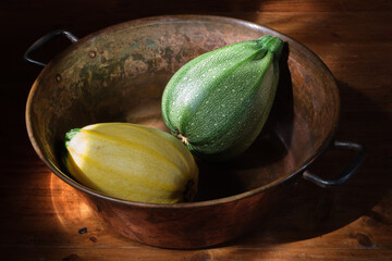 TWO Zucchini/courgette of different colors in a copper bowl on a wooden surface. The concept of harvesting, growing vegetables, breeding.