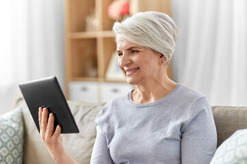 Fototapeta na wymiar technology, age and people concept - happy smiling senior woman with tablet pc computer at home