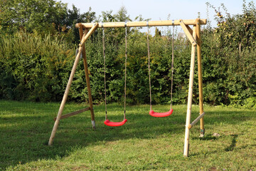 Children's swing made of logs and ropes and installed in the backyard of a rural house - obrazy, fototapety, plakaty