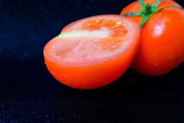 Ripe juicy red tomato with green leaves on a dark background. On tomatoes water drops, clean.