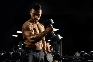 Fototapeta na wymiar Muscular bodybuilder training biceps with dumbbell.