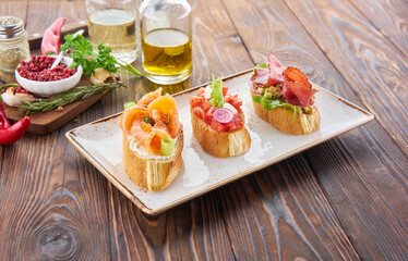 Bruschetta with various toppings, variety of small sandwiches with salmon red fish, fresh vegetables, tomatos and herbs on wooden table, diet food ingredients background.