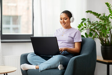 people, technology and leisure concept - happy young african american woman in headphones with laptop computer listening to music at home