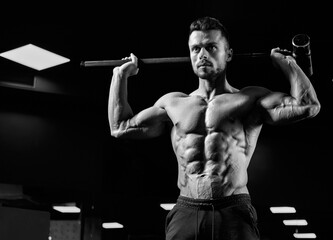 Muscular shirtless man holding sledgehammer in gym.