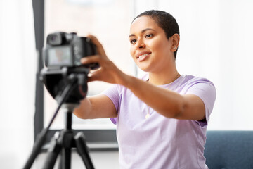 Fototapeta na wymiar blogging, videoblog and people concept - happy african american female video blogger adjusting camera on tripod at home