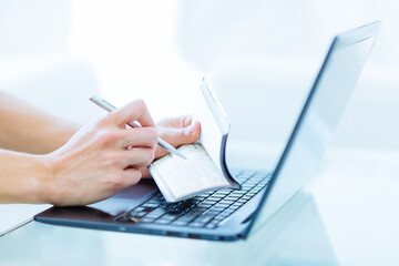 Close-up of a person's hands writing a bank cheque as a money transaction while online on a laptop...