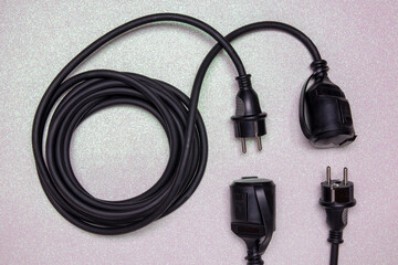 Closeup of a coiled black electric power extension cable with a further plug and socked on a bright glittering background. Space for design.