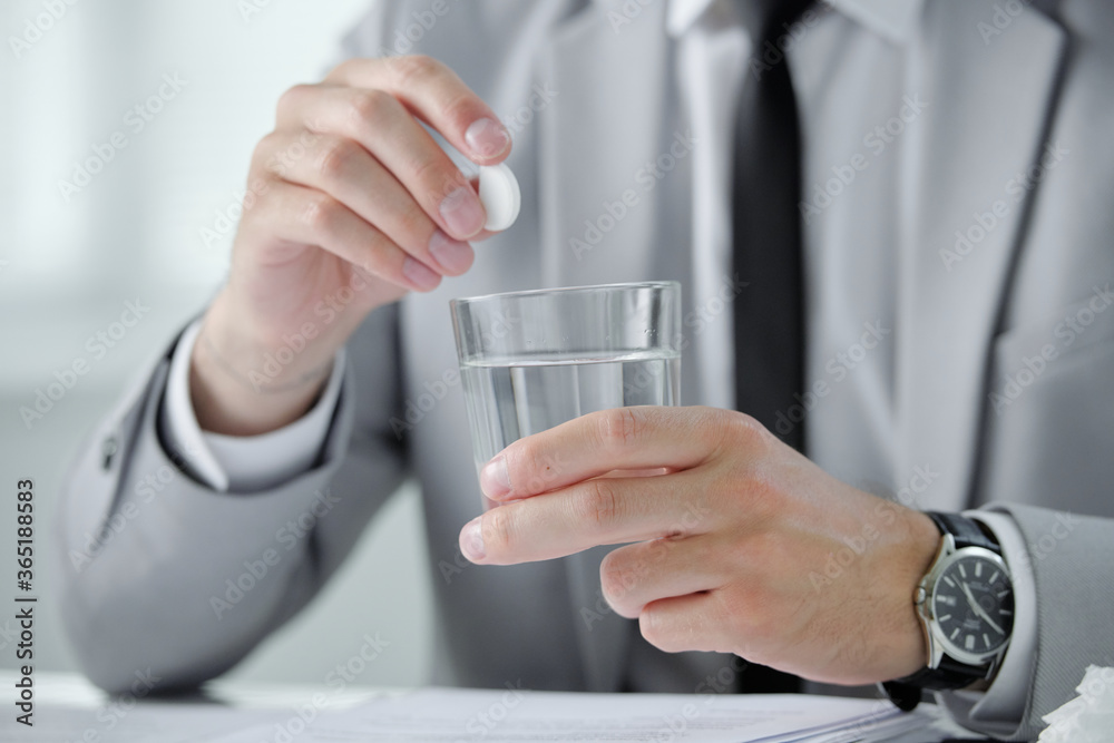 Poster Close-up of unrecognizable businessman in wristwatch dissolving pill into water while suffering from morning hangover at workplace