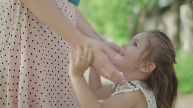 Unrecognizable mother touching face of smiling little Caucasian girl. Portrait of happy daughter looking up at parent and smiling. Joy, childhood, love, leisure, lifestyle.